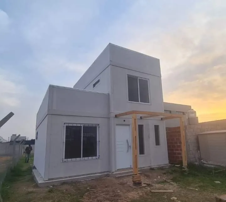 Fotografía de una vivienda de dos plantas en obra, con placas de cerramiento y pérgola de madera