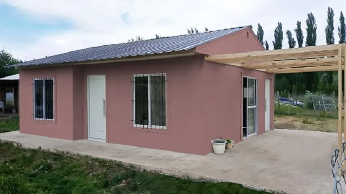 Casa Wood Frame color rosa con techo de chapa y pergolado de madera lateral, Geo Viviendas